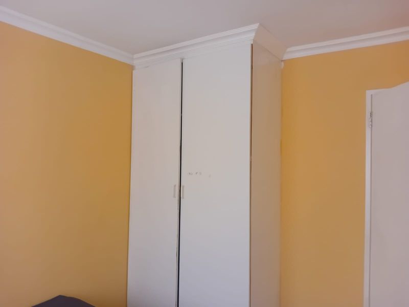 A bedroom corner featuring a built-in white wardrobe with crown molding detail against yellow painted walls.