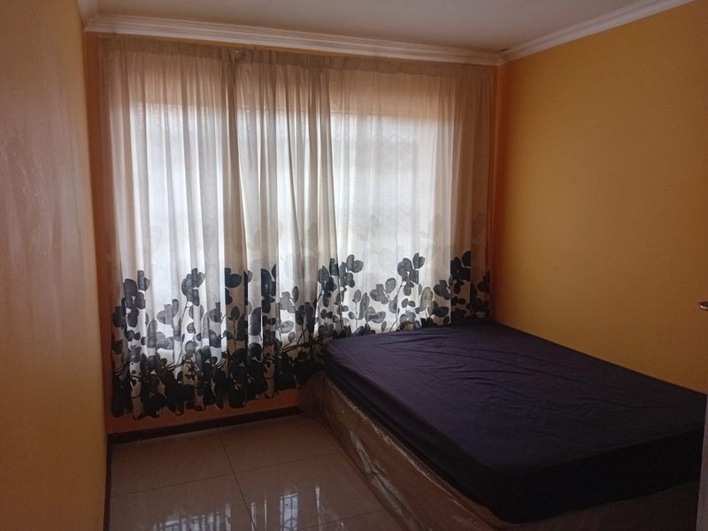 A bedroom featuring tiled flooring and large windows with curtain tracks, currently requiring cosmetic updates to the wall finishes.