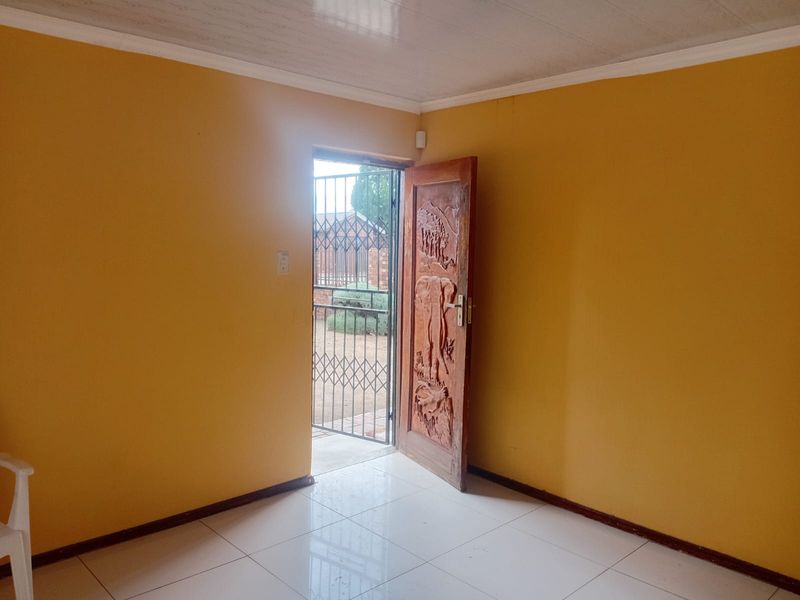 An empty entrance area featuring tiled flooring, a decorative carved wooden door, and a security gate leading to the exterior.