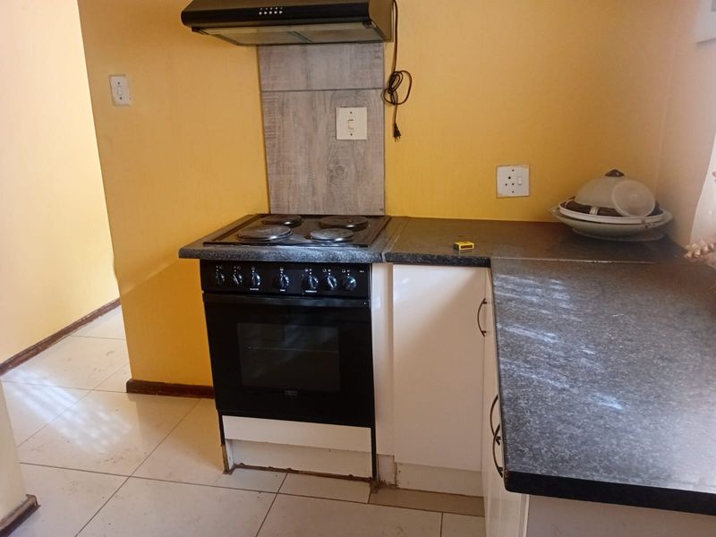 A compact kitchen area featuring a built-in electric stove, oven, extractor fan, and dark laminate countertops with tiled flooring.