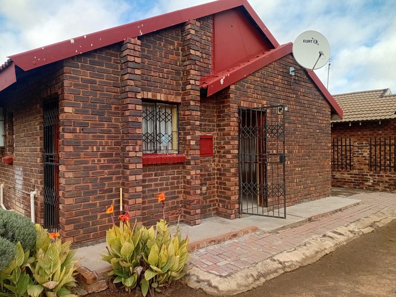 Front exterior view of a face brick house featuring metal security gates, a satellite dish, and a paved walkway.