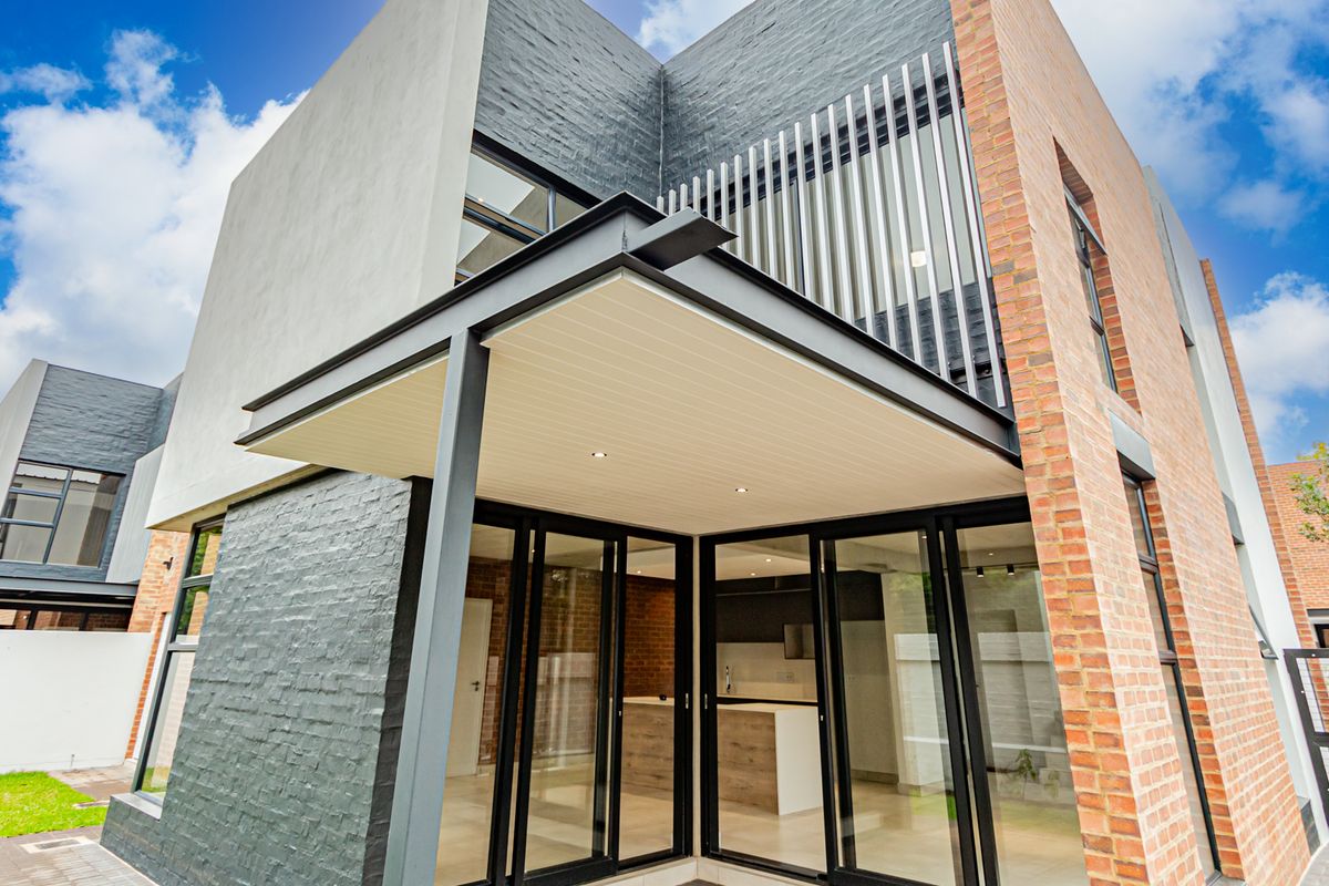 Modern townhouse rear elevation featuring a covered patio, large sliding glass doors, and a combination of face brick and painted brick finishes.