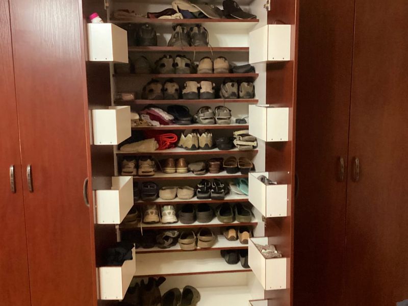A large built-in wooden wardrobe featuring extensive integrated shelving and storage compartments for organized clothing and footwear storage.