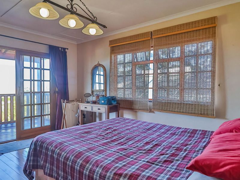 A bedroom featuring wooden flooring, multi-pane windows, and direct access to an outdoor balcony through glass-paneled french doors.
