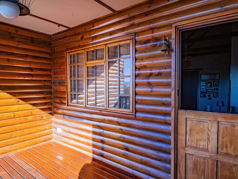 A covered timber deck featuring log wall cladding, wooden flooring, and a classic stable-style door leading into the interior.