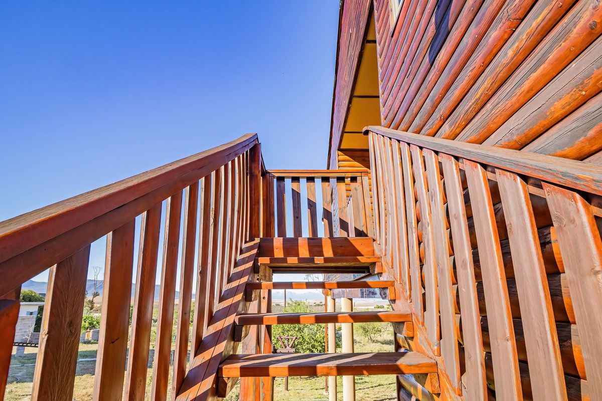 An exterior view of a log cabin featuring an elevated wooden staircase and balustrade leading to the upper level.