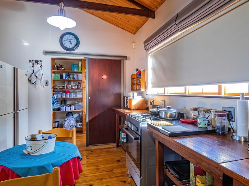 A rustic kitchen featuring timber flooring, exposed ceiling beams, wooden countertops, a gas stove, and a convenient walk-in pantry with a sliding door.