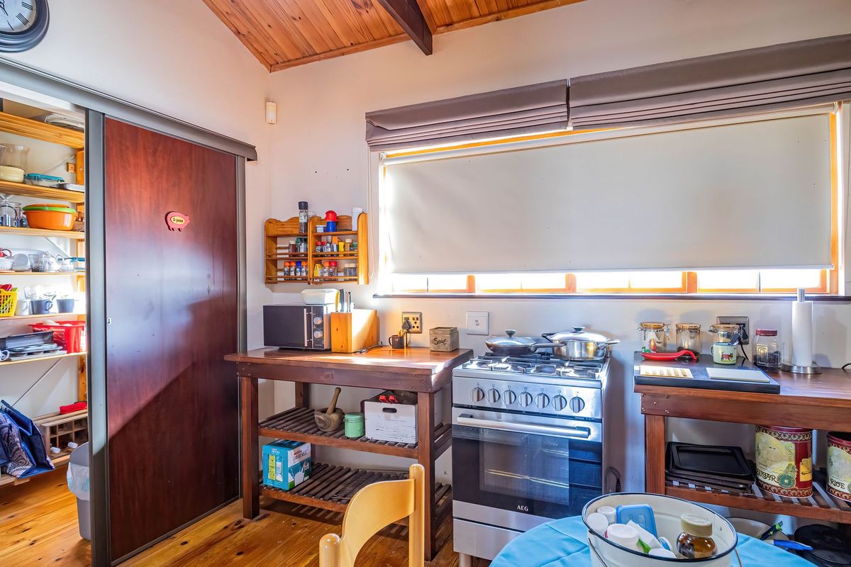 A rustic kitchen featuring timber ceilings and flooring, equipped with a gas stove and oven, complemented by an adjacent pantry area.