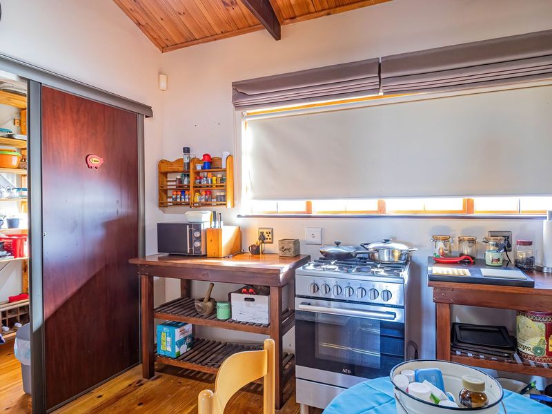 A rustic kitchen featuring timber ceilings and flooring, equipped with a gas stove and oven, complemented by an adjacent pantry area.