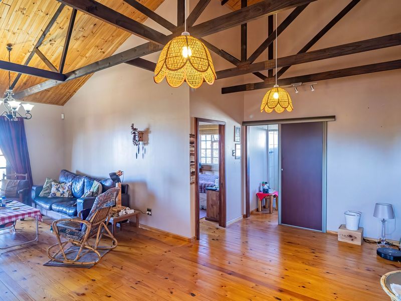 Spacious living area featuring high vaulted ceilings with exposed timber beams, warm timber flooring, and direct access to an outdoor balcony.