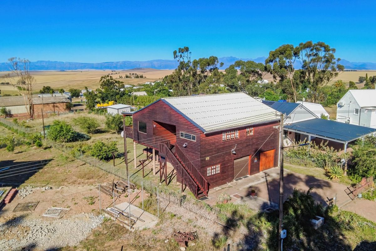 Aerial view of a two-story timber-clad house featuring a metal roof, elevated deck with external staircase, and ground-level garage access.