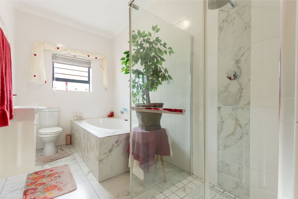 Modern bathroom featuring a glass-enclosed shower, a built-in bathtub with marble-look tiling, a pedestal basin, and a toilet.