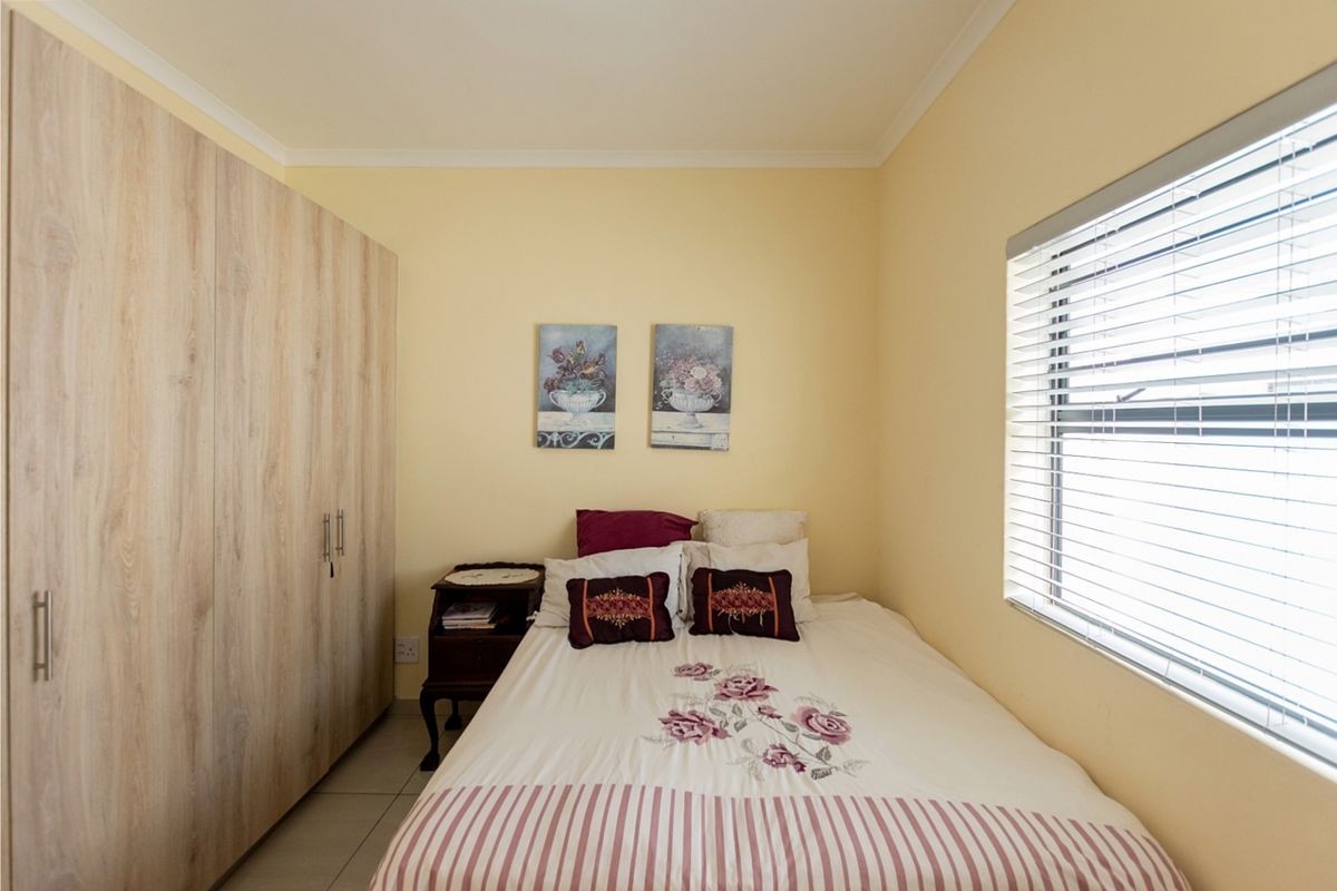A functional bedroom featuring light wood-finish built-in wardrobes, tiled flooring, and venetian blinds for privacy.