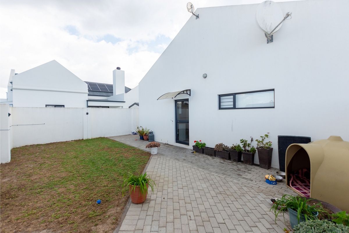 Rear exterior view featuring a paved patio area, white boundary walls, and a small lawn section.