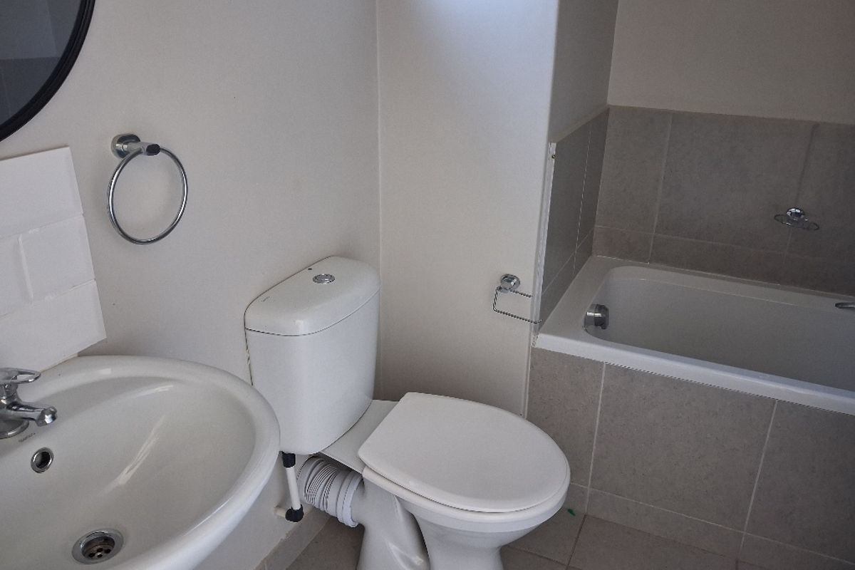 A functional bathroom featuring a pedestal basin, toilet, and a tiled built-in bathtub with neutral wall and floor finishes.