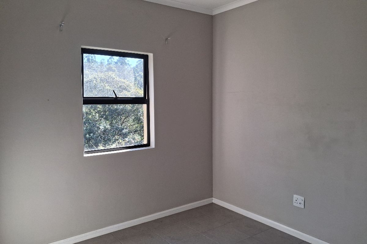 A clean, empty bedroom featuring neutral grey walls, tiled flooring, and an aluminium-framed window, providing a blank canvas for personalization.