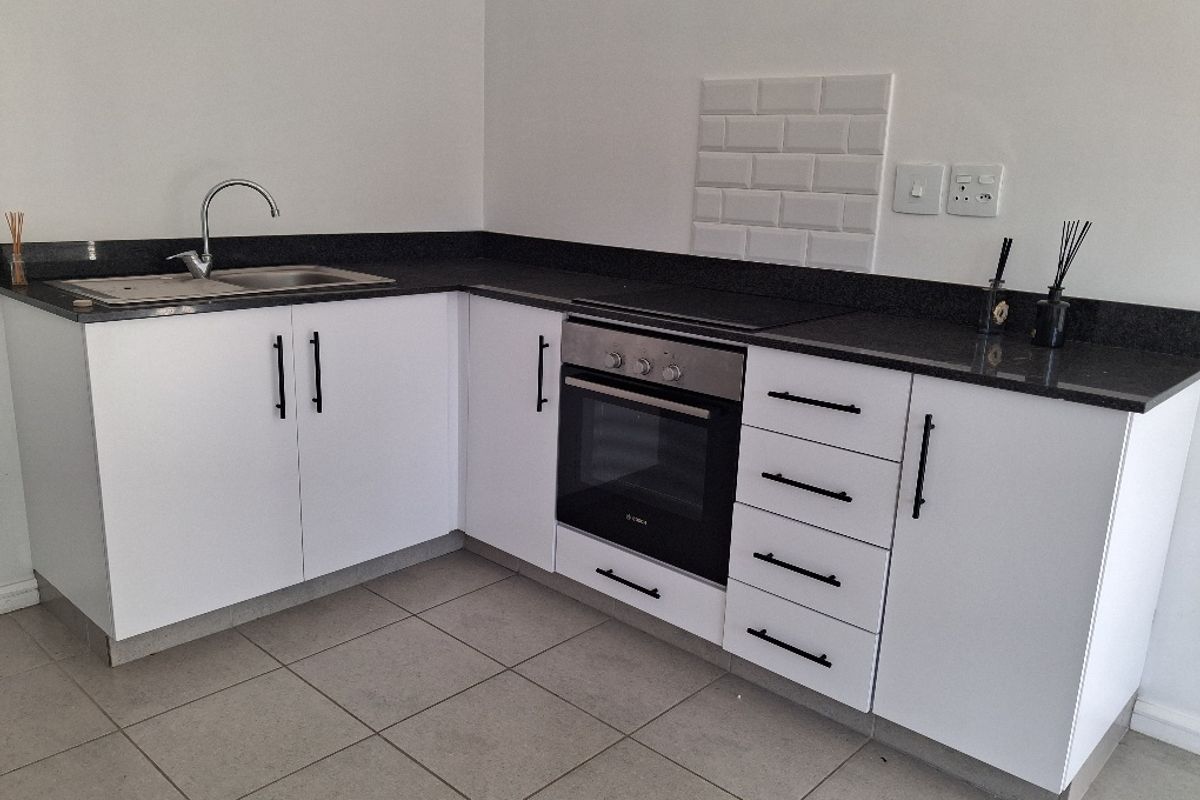 Modern kitchen featuring white cabinetry, dark granite countertops, built-in oven, hob, and a subway tile splashback with neutral tiled flooring.