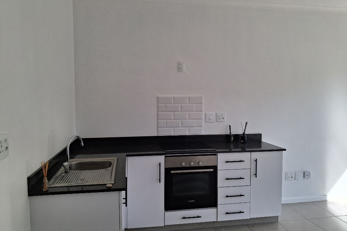 A clean, modern kitchen featuring white cabinetry, black granite countertops, a built-in oven, electric hob, and a stainless steel sink with subway tile splashback.