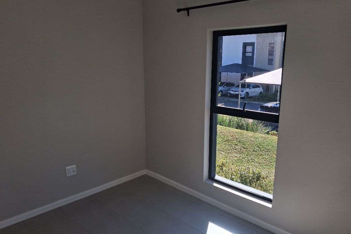 A clean, empty bedroom featuring neutral grey walls, tiled flooring, and an aluminium-framed window with a curtain rod.