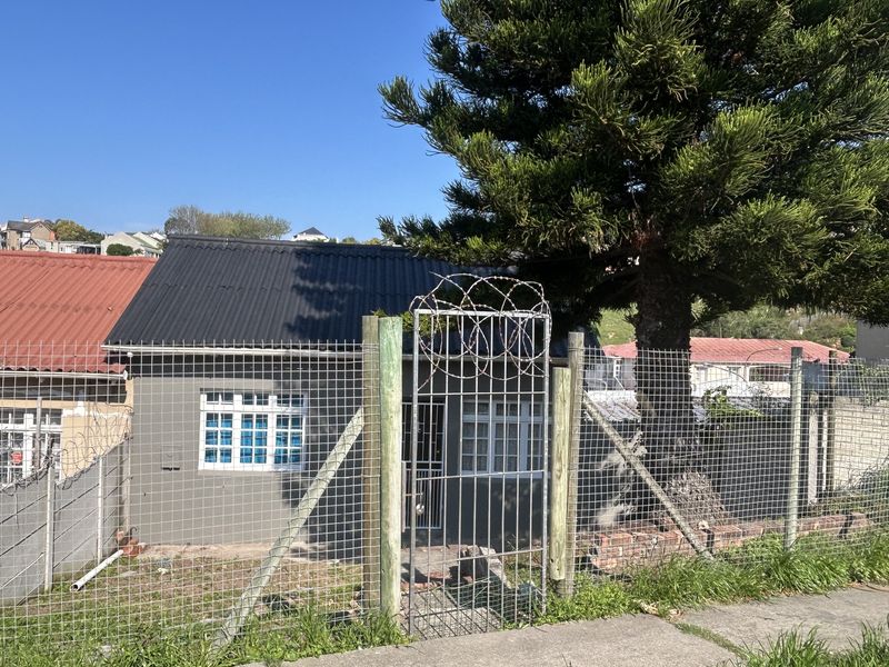 Front exterior view of a residential property featuring a corrugated metal roof, security fencing with razor wire, and a gated entrance.