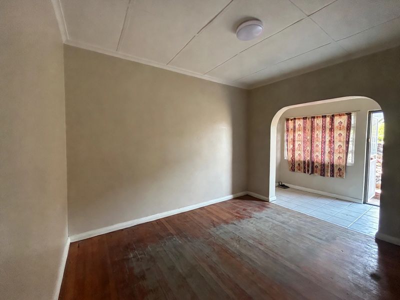 An empty living room featuring original hardwood flooring, a distinct archway leading to a tiled area, and neutral wall finishes.
