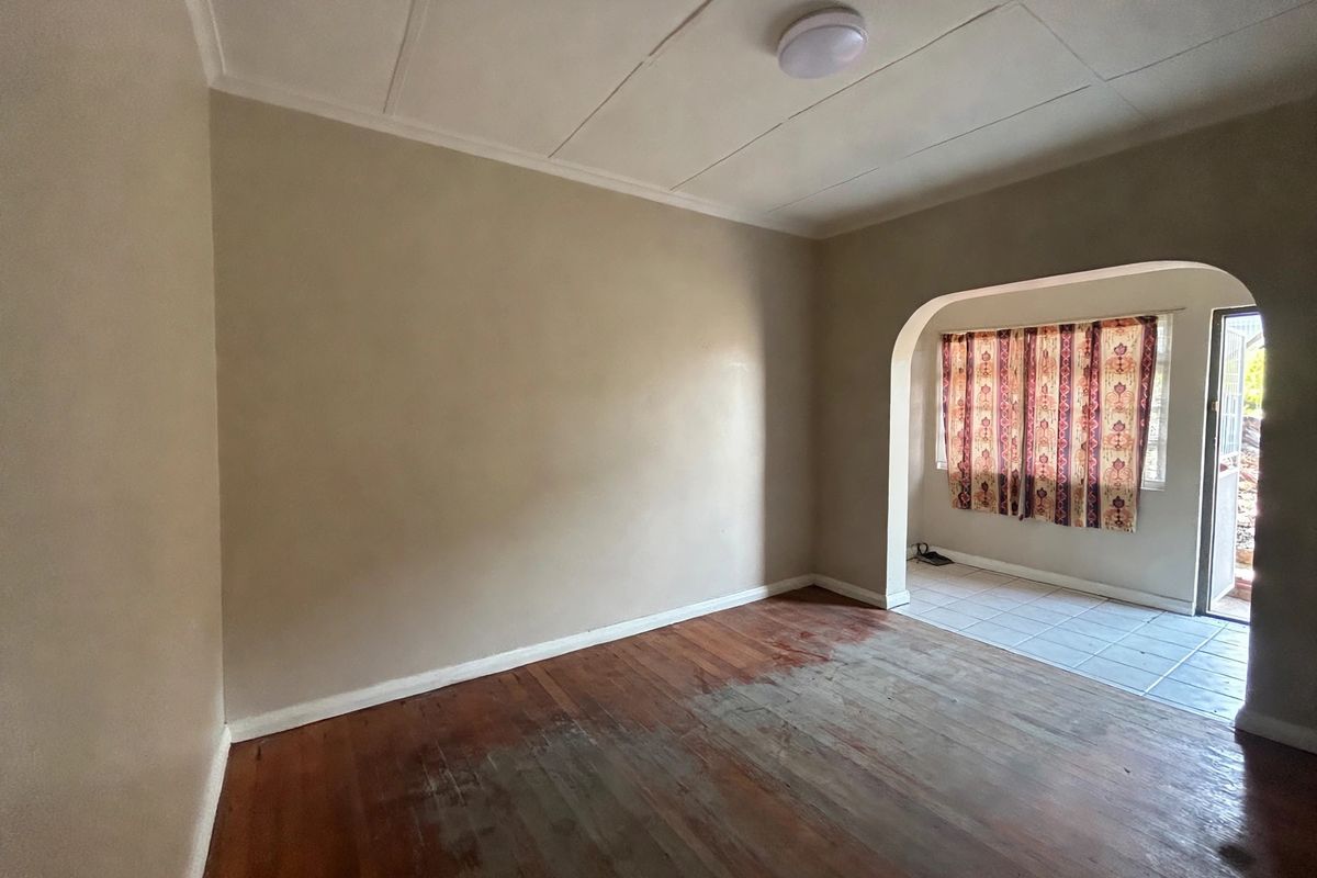 An empty living room featuring original hardwood flooring, a distinct archway leading to a tiled area, and neutral wall finishes.