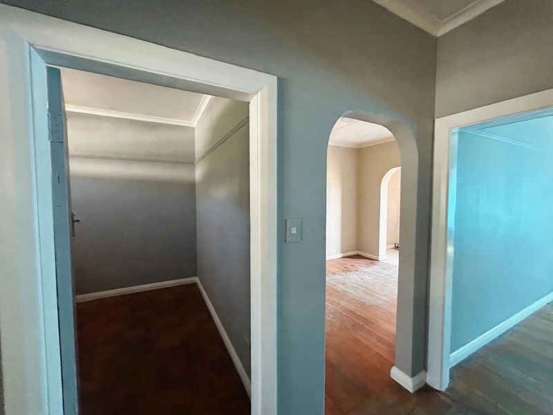 A vacant hallway featuring an arched doorway, parquet and timber flooring, and neutral wall finishes, providing access to multiple rooms.