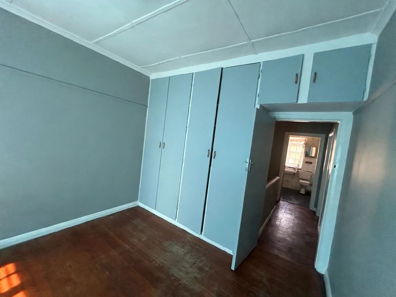 An empty bedroom featuring built-in cupboards, timber flooring, and a view into the adjacent bathroom.