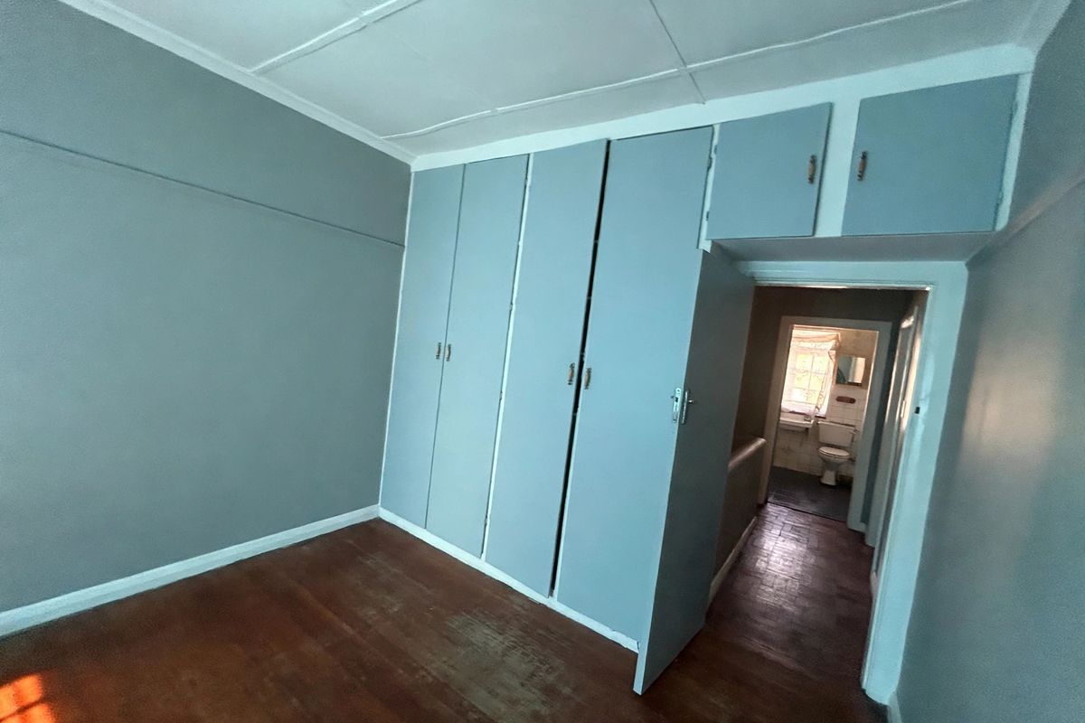 An empty bedroom featuring built-in cupboards, timber flooring, and a view into the adjacent bathroom.