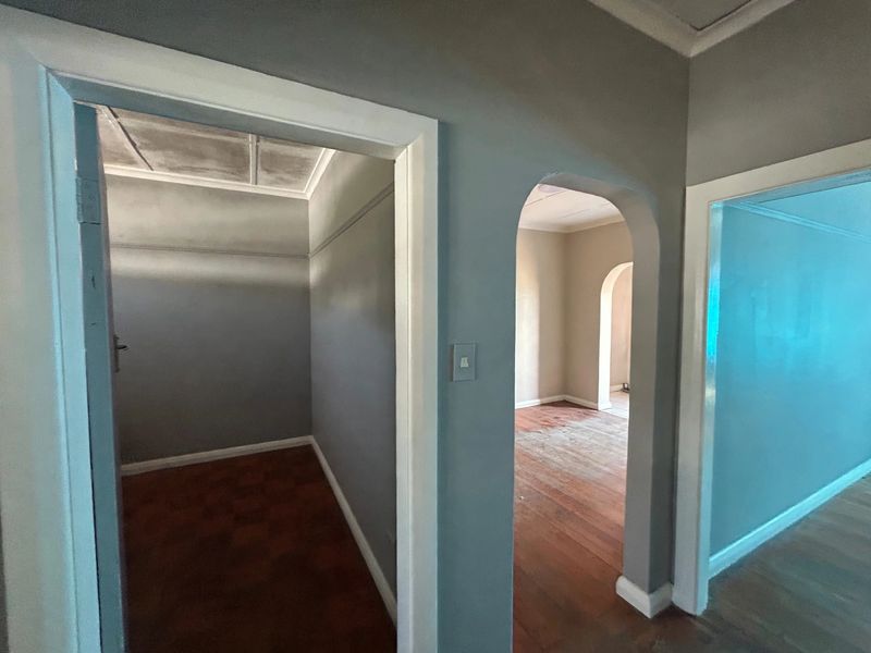 A view through a hallway featuring an arched doorway, parquet and timber flooring, and neutral wall tones, showing potential for interior updates.
