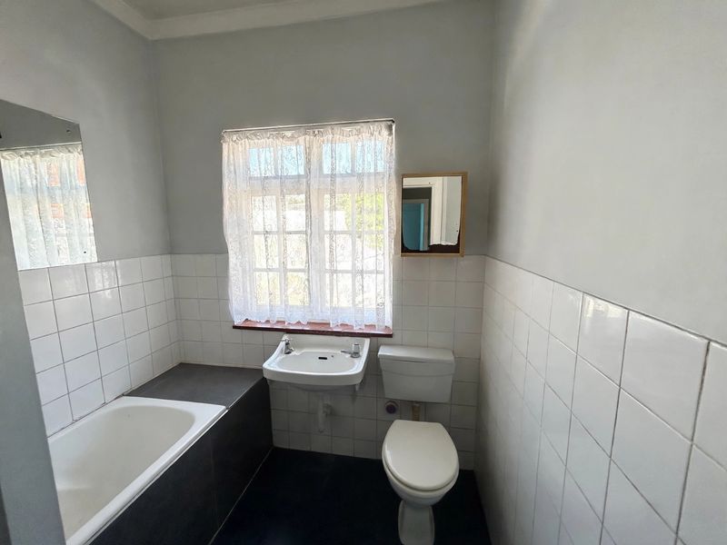 A functional bathroom featuring a built-in bathtub, wall-mounted basin, and toilet with white tiled splashbacks and neutral wall finishes.