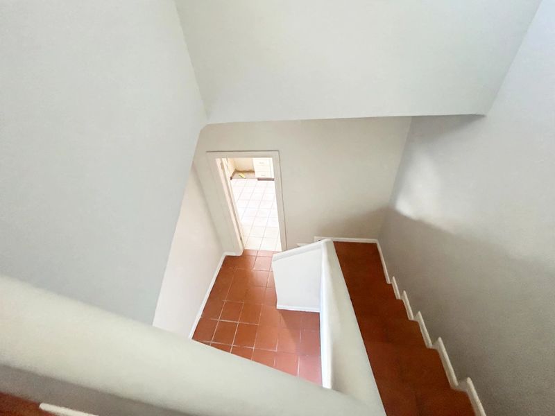 A view looking down a staircase with tiled steps and a solid balustrade, leading to an adjacent tiled room.