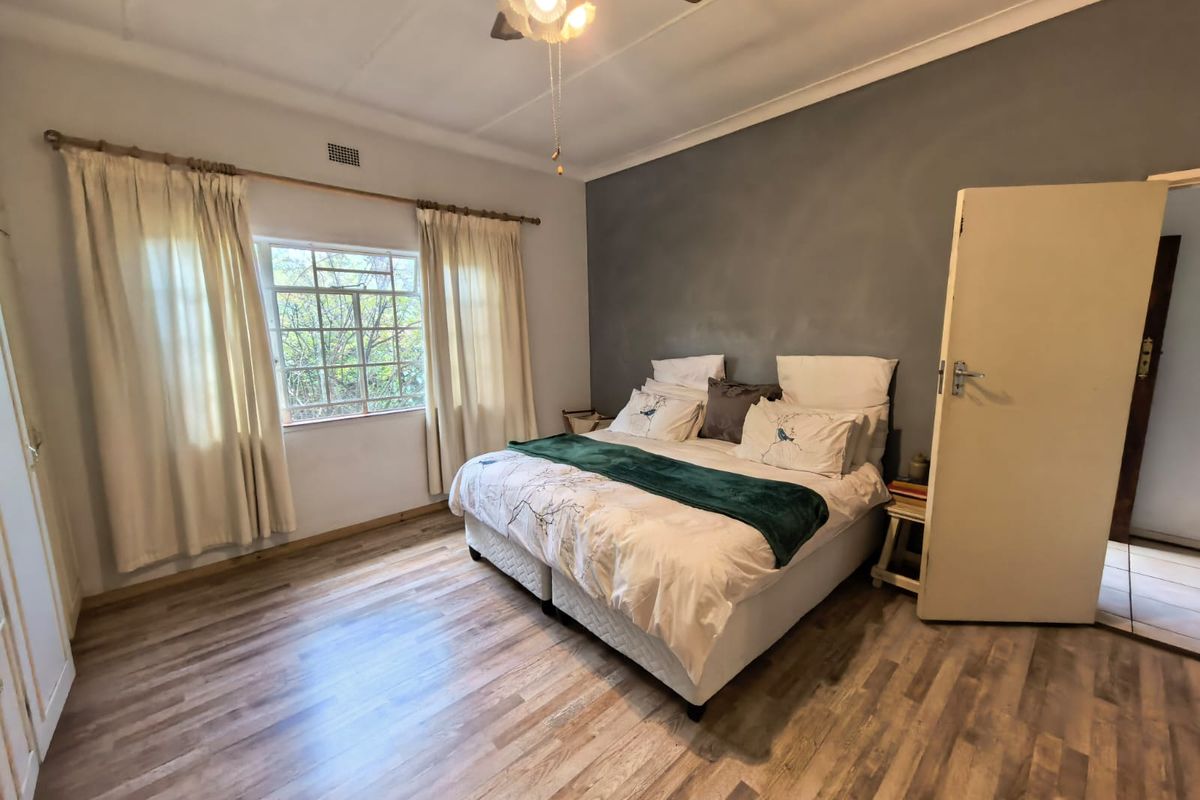 A bedroom featuring laminate flooring, a ceiling fan, and a feature wall, offering a functional space with potential for cosmetic updates.