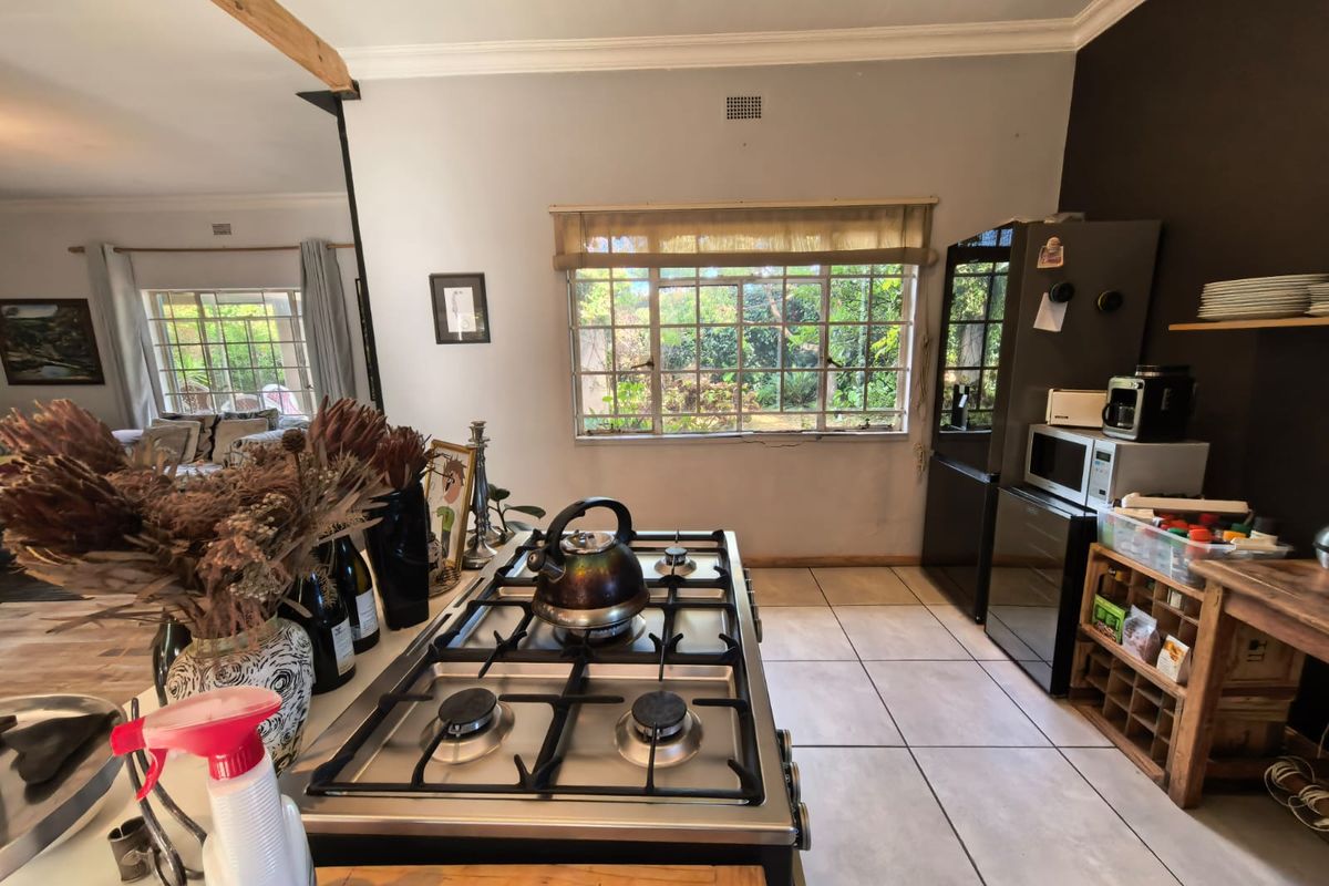 A functional kitchen featuring a gas hob, tiled flooring, and a timber ceiling beam, with an open-plan layout connecting to the adjacent living area.