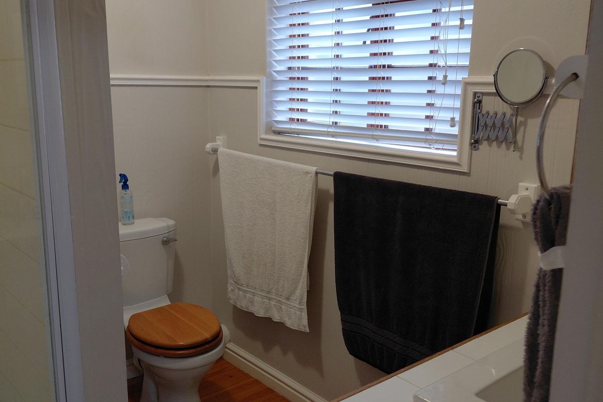 A functional bathroom featuring a shower enclosure, toilet, and a tiled vanity basin with timber flooring and wall panelling details.