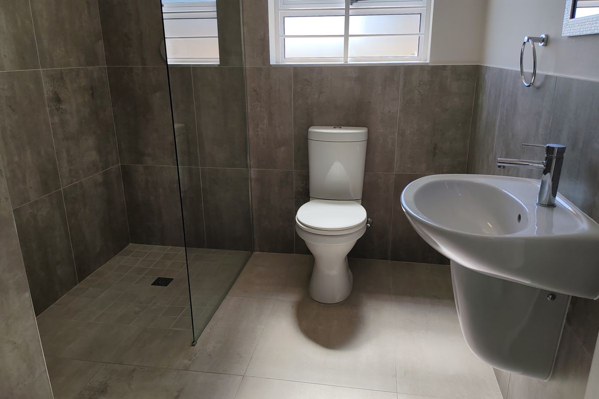 Modern bathroom featuring a walk-in glass shower, pedestal basin, and toilet with contemporary grey wall tiling and neutral floor tiles.