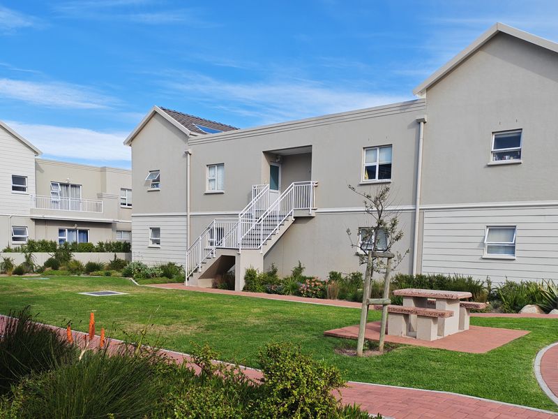 A well-maintained residential complex featuring a communal lawn, paved pathways, and external staircases providing access to upper-level units.