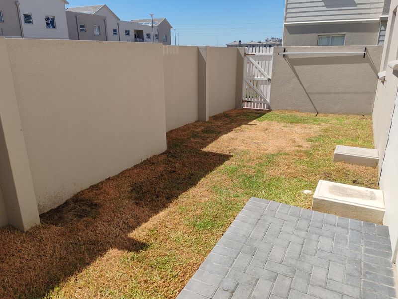 A private rear garden area featuring a paved patio, boundary walls, a pedestrian gate, and a wall-mounted washing line.