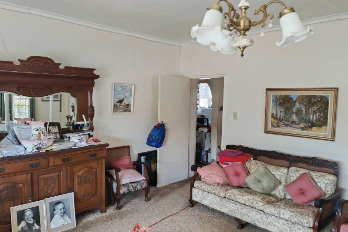 A traditional living room featuring a classic chandelier, ceiling rose, and an archway leading to an adjacent space, showing signs of wear.