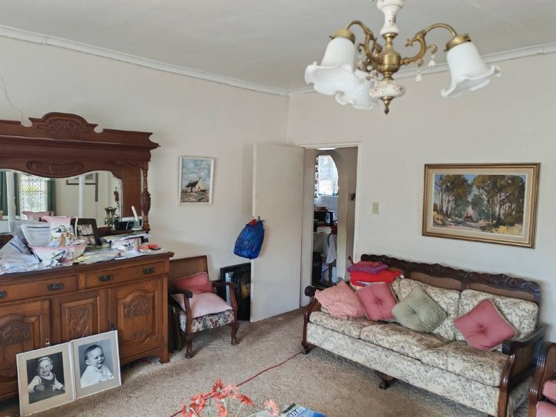 A traditional living room featuring a classic chandelier, ceiling rose, and an archway leading to an adjacent space, showing signs of wear.