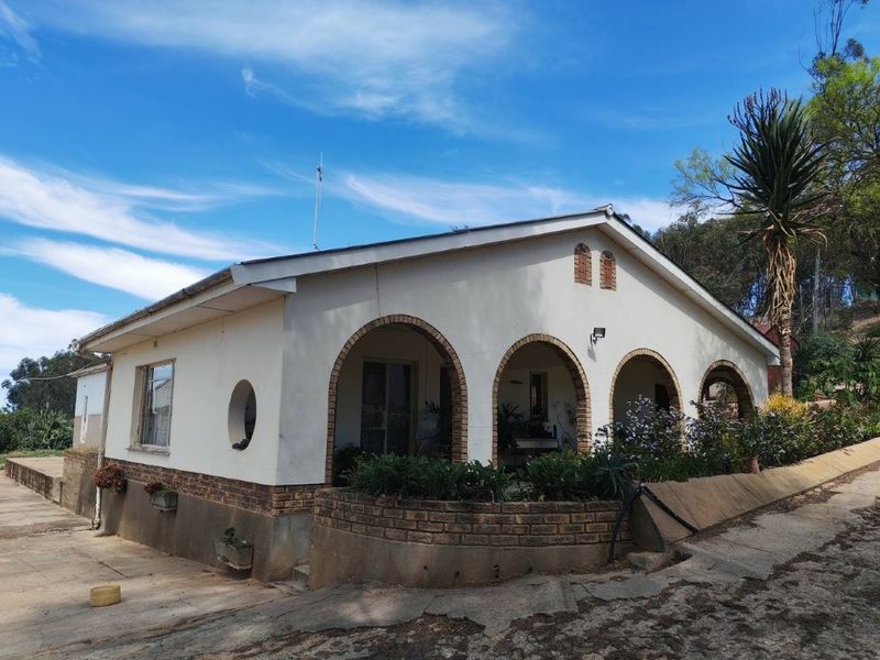 A farm-style residence featuring a covered arched veranda, brick accents, and a concrete driveway, set against a rural landscape.