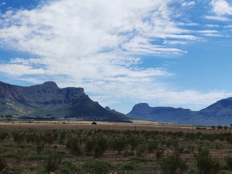 Expansive scenic view of the surrounding mountain range and open farm landscape under a clear blue sky.