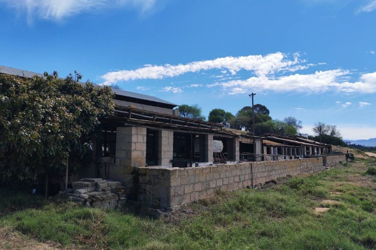A large, dilapidated agricultural outbuilding or barn structure featuring concrete block walls and a corrugated metal roof, requiring significant restoration or redevelopment.