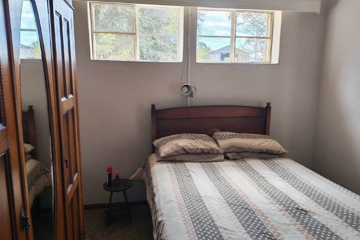 A functional bedroom featuring carpeted flooring and dual casement windows, providing natural light and a view of the surrounding farm landscape.
