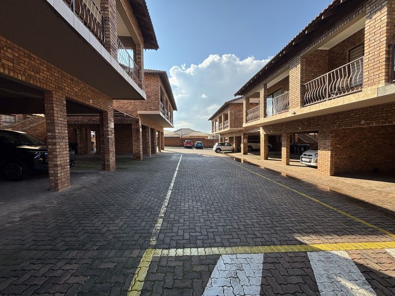 Exterior view of a townhouse complex featuring brick facades, covered parking bays, and upper-level balconies with metal railings.
