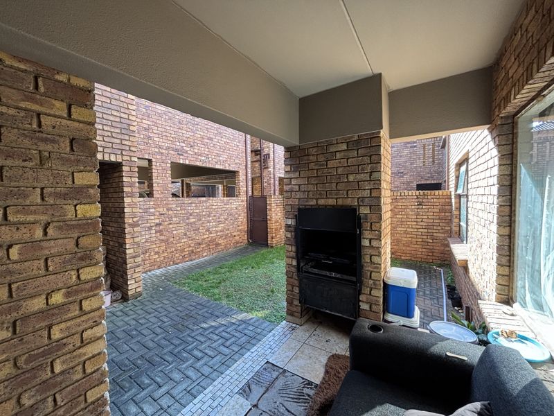 A covered patio area featuring exposed brickwork, paved flooring, and a built-in braai, overlooking a small private courtyard garden.