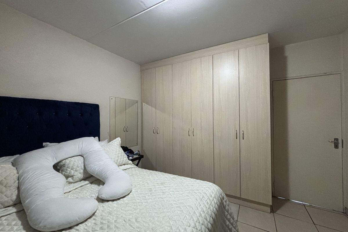 A bedroom featuring light wood-finish built-in cupboards, tiled flooring, and a standard internal door.