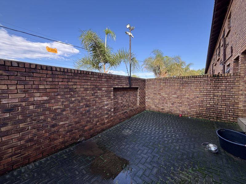 A private rear courtyard featuring brick boundary walls, paved flooring, and integrated security lighting and surveillance equipment.