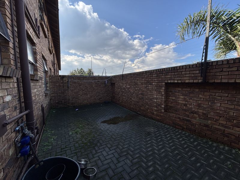 A private rear courtyard featuring brick boundary walls with electric fencing and paved flooring, providing a secure and functional outdoor utility space.