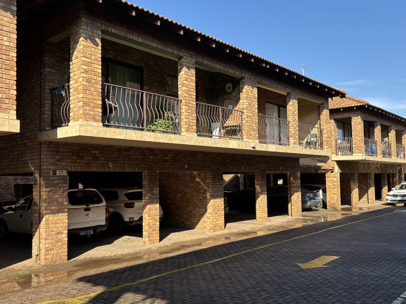 Exterior view of a face brick townhouse complex featuring covered ground-level parking bays and upper-level balconies with wrought iron railings.
